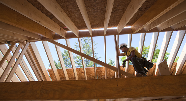 Hispanic carpenter with a circular saw on rafter at a house under construction