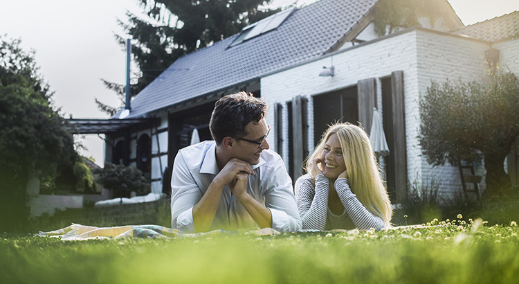 Happy mature couple lying on meadow in front of their house